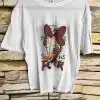 Zeig deinen Style und gute Laune mit dem Daisy Power Shirt! Der süße Cartoon-Print einer Ente mit roter Schleife verleiht deinem Look das gewisse Etwas. Vor der coolen Steinwand wirkt das Shirt besonders modern - kombiniere es zu Jeans oder Rock und bringe Farbe in deinen Alltag. Mit diesem Statement-Shirt ziehst du garantiert alle Blicke auf dich!.