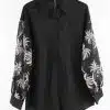 Mit der "Tropical Elegance" Bluse hebst du deinen Look hervor - stylisches Schwarz, weiße Palmenmotive, modern am Bügel inszeniert.