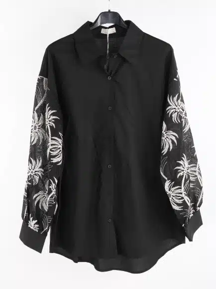 Mit der "Tropical Elegance" Bluse hebst du deinen Look hervor - stylisches Schwarz, weiße Palmenmotive, modern am Bügel inszeniert.
