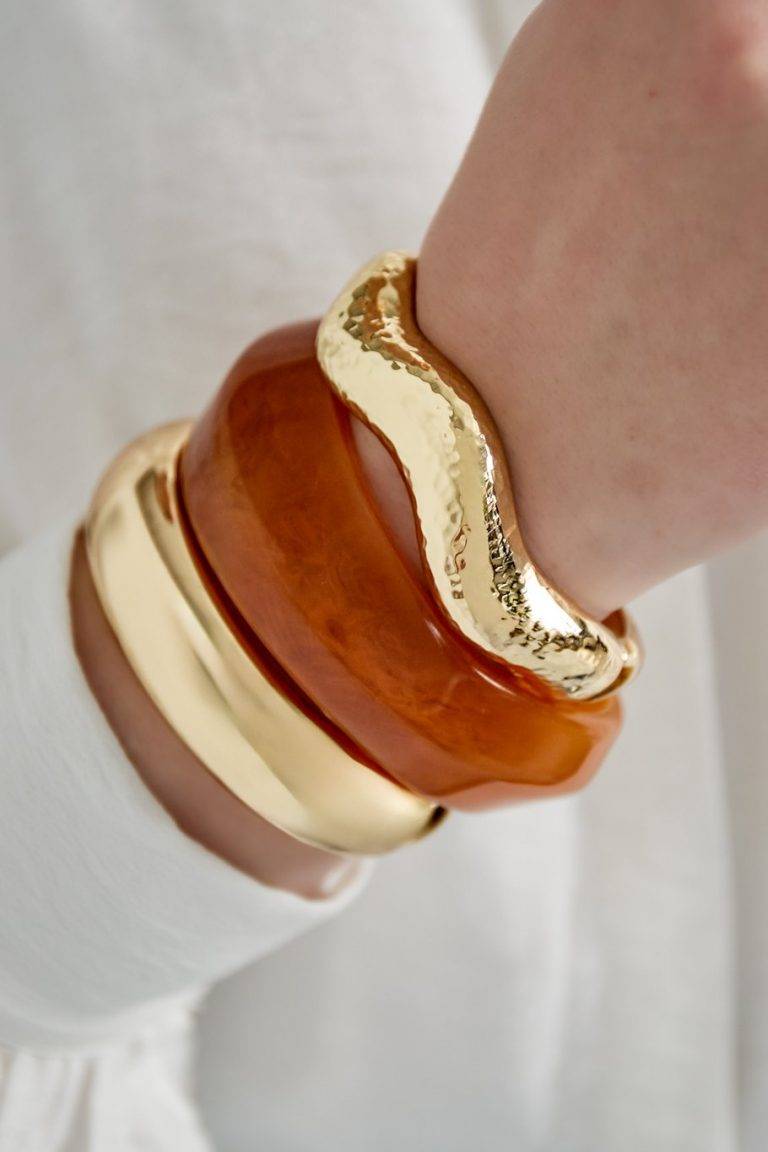 Stecke dein Handgelenk in Szene - goldene und bernsteinfarbene Statement-Bangles über deinem weißen Longsleeve, ready to shine!.