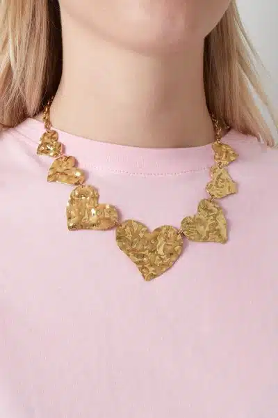 Trage ein pinkes Shirt und verleihe deinem Look mit einer goldenen Halskette voller gehämmerter Herzanhänger modernen Glam.