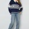 Setze ein Statement mit deinem navy "LOS ANGELES" Pulli, Jeans mit Perlen-Details und pinken Schuhen vor hellem Hintergrund.