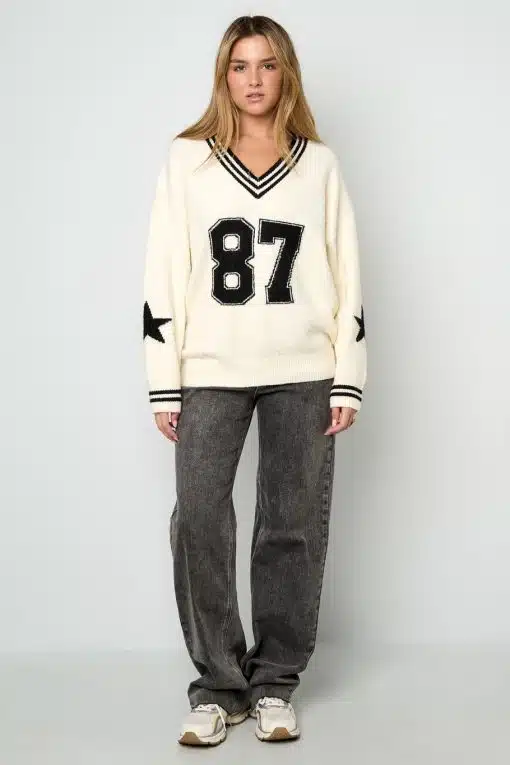Zeig deinen Style mit dem cremefarbenen Varsity Star Pulli, grauen Jeans und coolen Sneakern vor cleanem, weißem Hintergrund.