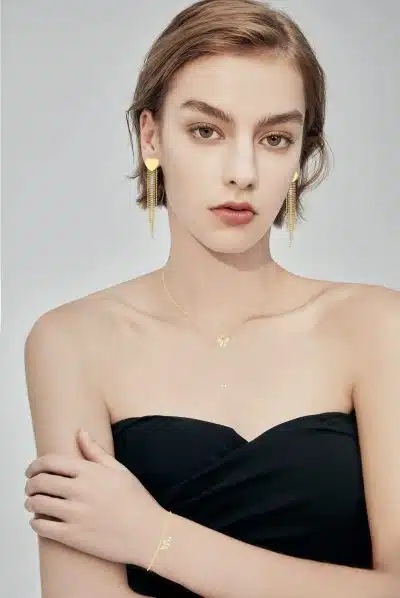 Erlebe deinen modernen Look: In schwarzem Top setzt du mit goldenen Heart Tassel Ohrringen, Kette und Armband elegante Akzente.