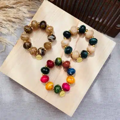 Entdecke deinen Style: Vier bunte Perlenarmbänder mit edlen Goldanhängern warten auf dich, stilvoll präsentiert auf Holz.