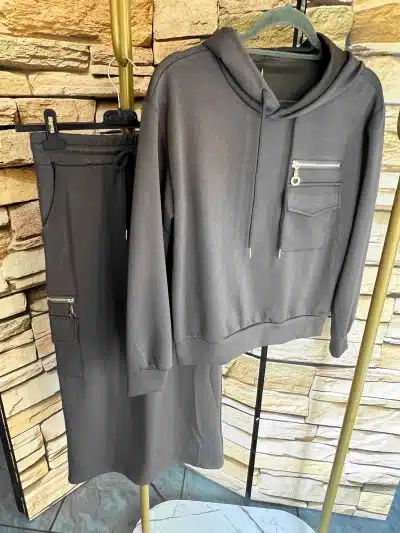 Erlebe ultimativen Komfort: Das Urban Comfort Set - grauer Hoodie und passender Rock mit Zipper-Taschen vor Stone-Wall-Design.