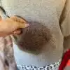 Du hältst einen flauschigen, braunen Pom-Pom an deiner grauen Chic Fur Touch Pulli-Tasche - der moderne Must-Have-Look!.