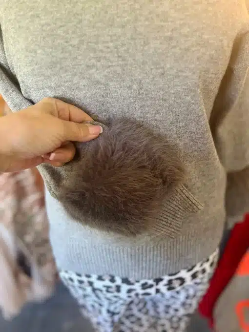 Du hältst einen flauschigen, braunen Pom-Pom an deiner grauen Chic Fur Touch Pulli-Tasche - der moderne Must-Have-Look!.
