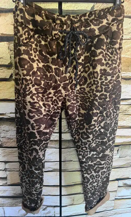 Erlebe die zauberhafte Velour Wild Jogpants im braunen Leopardenmuster - stilvoll inszeniert vor einer hellen Steinwand!.