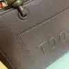 Erlebe das moderne Design der "Toos" Handtasche: edle braune Textur, runde Griffe und stilvoll geprägtes Logo.