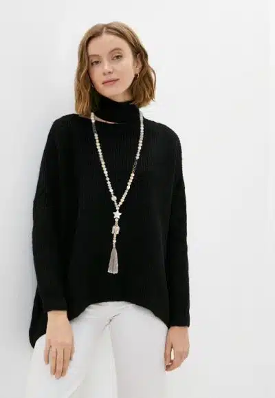 Setze ein Statement: Du trägst einen schwarzen Rollkragenpullover, weiße Hosen und eine lange, trendige Kette mit Quaste.