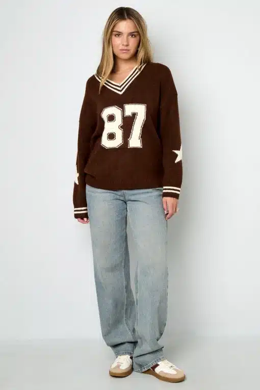 Style den angesagten Varsity Star Pulli in Braun mit "87" und deinen hellblauen Jeans für einen freshen Look vor weißer Wand.