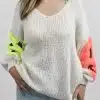 Erlebe den SMILY Pulli an dir: Cremefarbener Strick, leuchtend gelbe und pinke Ärmel - dein Must-have vor schlichter Kulisse.