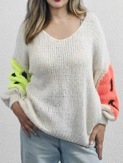 Erlebe den SMILY Pulli an dir: Cremefarbener Strick, leuchtend gelbe und pinke Ärmel - dein Must-have vor schlichter Kulisse.