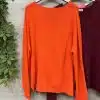 Entdecke deinen neuen Lieblingspullover: Ein leuchtender oranger Sweater neben einem burgundroten Akzent an einer Holz-Wand.