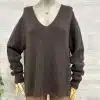 Entdecke deinen neuen Look: Lockerer, dunkelbrauner V-Neck-Sweater und angesagte beigefarbene Hosen vor hellem Holz.