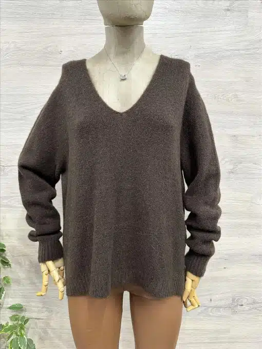 Entdecke deinen neuen Look: Lockerer, dunkelbrauner V-Neck-Sweater und angesagte beigefarbene Hosen vor hellem Holz.