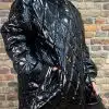 Du trägst den Glossy Oversize Coat, schwarze Leggings und weiße Sneaker - stylisch vor einer angesagten Backsteinwand.