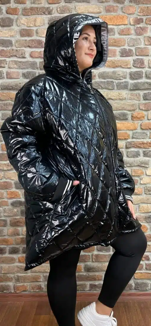 Du trägst den Glossy Oversize Coat, schwarze Leggings und weiße Sneaker - stylisch vor einer angesagten Backsteinwand.