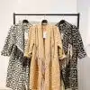 Entdecke deinen Look: Stilvolle "Ethno Style Coat"-Jacken mit Fransen in Schwarz, Beige und Weiß warten auf dich am Kleiderständer.