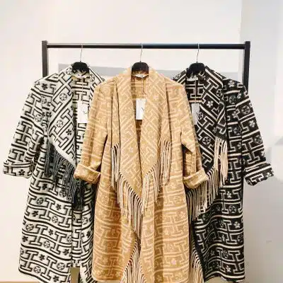 Entdecke deinen Look: Stilvolle "Ethno Style Coat"-Jacken mit Fransen in Schwarz, Beige und Weiß warten auf dich am Kleiderständer.