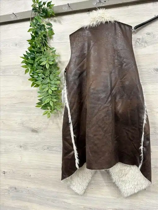 Du hängst Urban Chic an die Wand: Die braune Kunstleder-Weste mit weißem Fellfutter neben grünen Pflanzen - stylisch und modern!.
