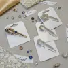 Entdecke die Shine & Chic Ponchonadel: Glitzernde Sicherheitsnadeln mit Edelsteinen, stilvoll auf Stoff, Spitze und Juwelen inszeniert.