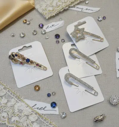 Entdecke die Shine & Chic Ponchonadel: Glitzernde Sicherheitsnadeln mit Edelsteinen, stilvoll auf Stoff, Spitze und Juwelen inszeniert.