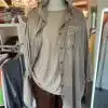 Entdecke die "Peace & Wings Blusenjacke" - glänzend, edel in Beige, mit trendigem Kragen, über Nieten-Top und Braune Hose gestylt.