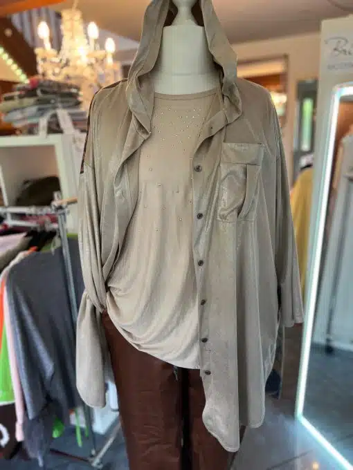 Entdecke die "Peace & Wings Blusenjacke" - glänzend, edel in Beige, mit trendigem Kragen, über Nieten-Top und Braune Hose gestylt.