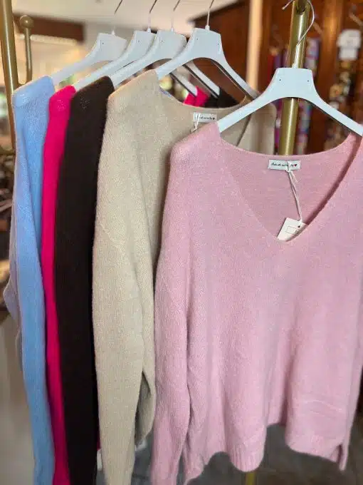 Entdecke deinen Style: Sechs bunte Pullover auf weißen Bügeln, die vorne pinke, frische Farben warten auf dich!.