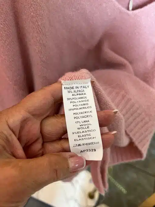 Du hältst einen stylishen pinken Pullover in der Hand - das Label verrät dir Materialmix und smarte Pflegehinweise.