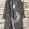 Entdecke deinen neuen Look: Der Ethno Style Coat - schwarz-weiß gemustert, mit stylischem Fransen-Detail am coolen Steinwall.