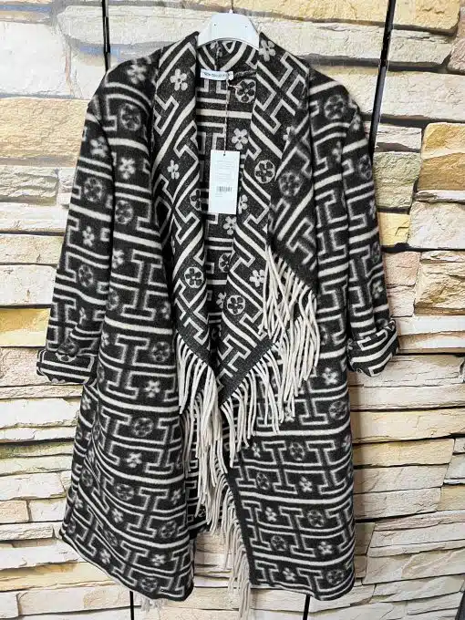 Entdecke deinen neuen Look: Der Ethno Style Coat - schwarz-weiß gemustert, mit stylischem Fransen-Detail am coolen Steinwall.