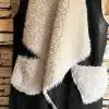 Erlebe deinen Style neu: Die schwarze Urban Chic Wendeweste mit weißem Webpelzkragen setzt dich vor Steinwand perfekt in Szene.
