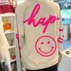 Hol dir das stylische "Be Happy" Sweatshirt in Beige - hinten mit "hap-" und einem pinken Smiley mit Sternaugen als Eyecatcher!.