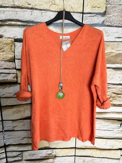 Zieh dir das angesagte orange "Basic Deluxe - Shirt mit Kette" an: stylisch, modern, ein echter Eyecatcher vor Steinwand!.