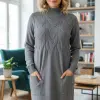 Du trägst das Cable Chic Dress in einem stylischen, gemütlichen Wohnzimmer mit Bücherregalen und üppigen Pflanzen.