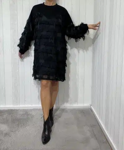 Du strahlst in deinem schwarzen, strukturierten Kleid und angesagten Ankle Boots vor der stylischen weißen Paneelwand.