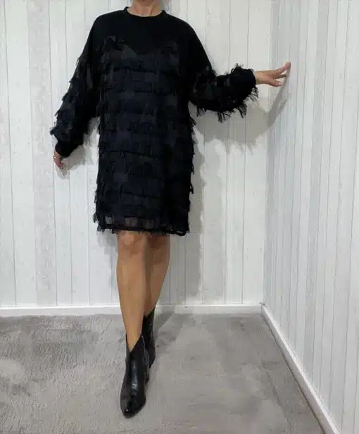 Du strahlst in deinem schwarzen, strukturierten Kleid und angesagten Ankle Boots vor der stylischen weißen Paneelwand.