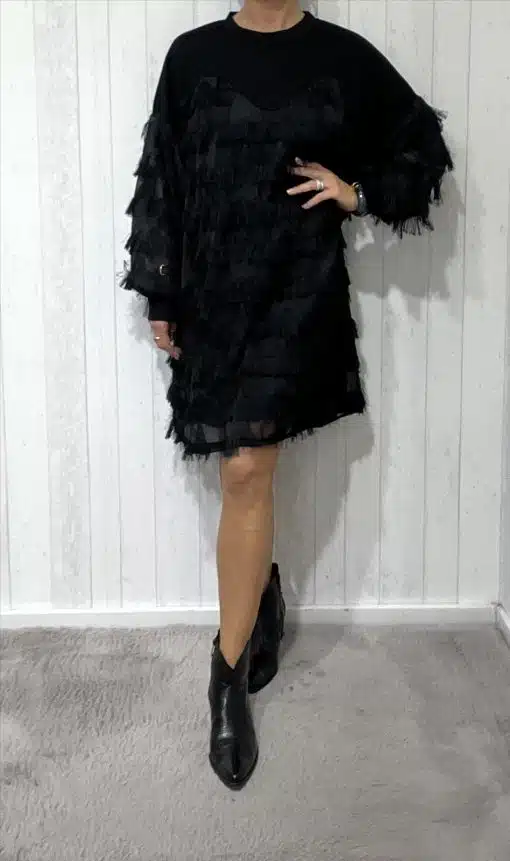Du trägst ein schwarzes Fransen-Kleid mit langen Ärmeln und stylischen Ankle Boots - ein moderner Look vor hellem Hintergrund.