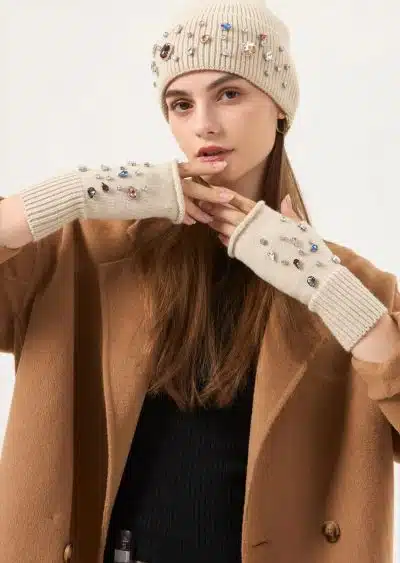 Du trägst einen schicken beigen Mantel, eine cremefarbene Schmuck-Beanie und passende Fingerhandschuhe - dein moderner Look.