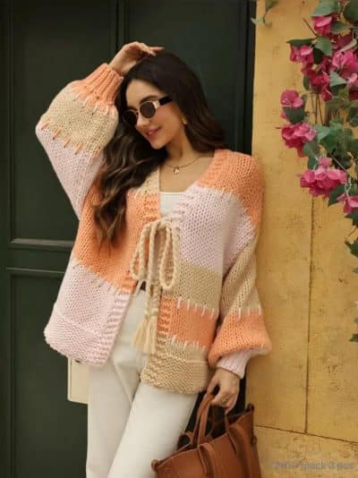 Du trägst stylische Sonnenbrillen, einen modernen Strickcardigan in Pfirsich-Beige und deine Trend-Bag vor der grünen Tür.