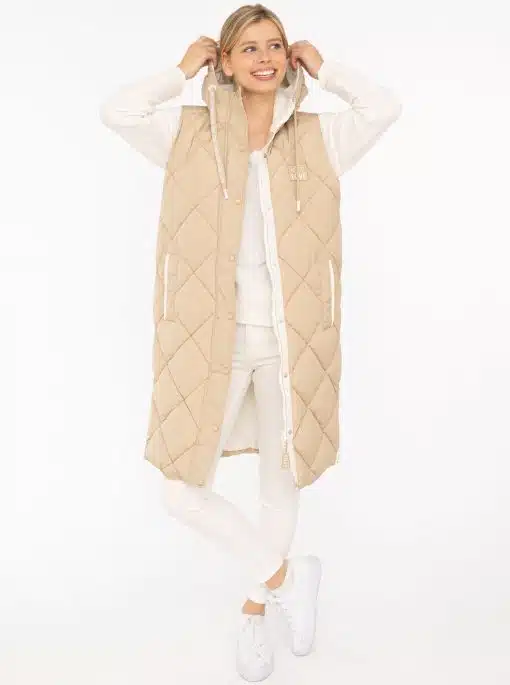 Du trägst eine lange beige Steppweste über weißem Outfit, lächelst und hältst cool die Kapuze - bereit für deinen modernen Look.