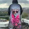 Du trägst einen stylischen Kapuzenmantel mit buntem Geparden- und Pink-Design, stehst cool auf einem Rooftop und blickst hinaus.