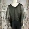 Entdecke die Wild Clash Tunika: Du trägst die transparente, schwarze It-Piece-Bluse mit Statement-Ärmeln vor edlem Setting.