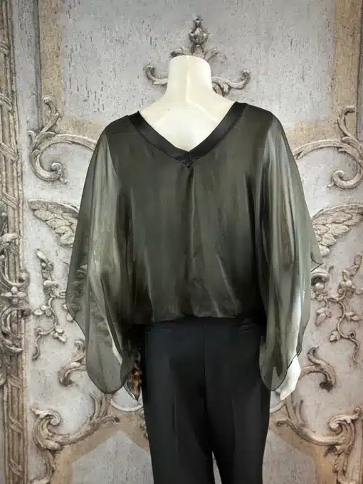 Entdecke die Wild Clash Tunika: Du trägst die transparente, schwarze It-Piece-Bluse mit Statement-Ärmeln vor edlem Setting.