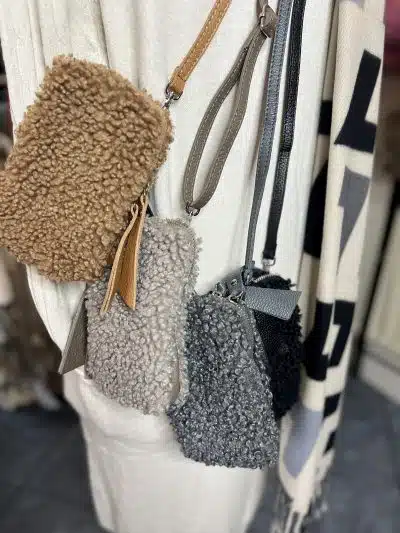 Entdecke deinen Style: Die kleinen, flauschigen Teddy Taschen in Braun, Grau und Schwarz warten am Kleiderständer auf dich!.