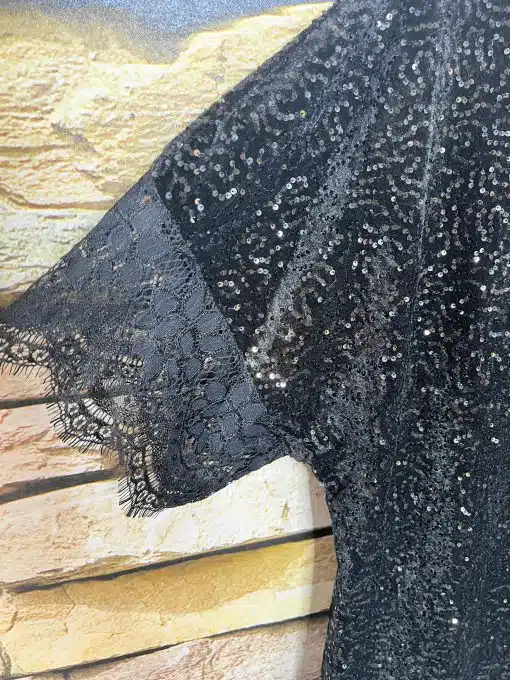 Erlebe das Gala Shine Kleid - ein funkelndes Paillettenkleid mit Schleife und Spitzenärmeln vor trendiger gelber Backsteinwand.