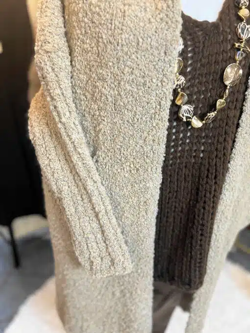 Erlebe den Alpaca Dream Cardigan in beigem Strick, lässig über braunem Pullover, veredelt mit gold-brauner Statement-Kette.